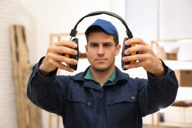 Worker holding safety headphones indoors, focus on hands. Hearing protection device