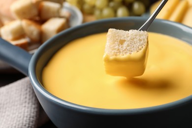 Dipping piece of bread into tasty cheese fondue, closeup