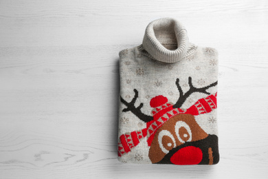 Folded warm Christmas sweater with deer on white table, top view. Space for text