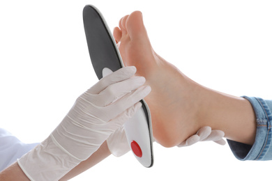 Orthopedist fitting insole on patient's foot against white background, closeup