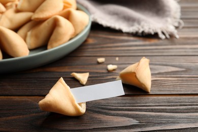 Tasty fortune cookies and paper with prediction on wooden table, space for text