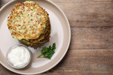 Delicious zucchini fritters with sour cream served on wooden table, top view. Space for text