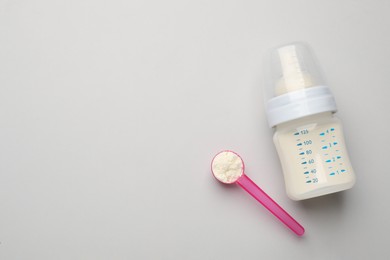 Feeding bottle with infant formula and powder on light background, flat lay. Space for text
