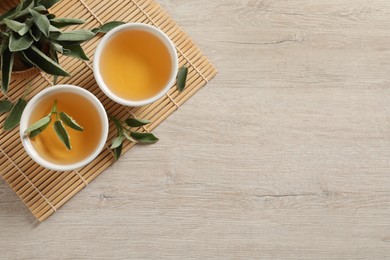 Aromatic sage tea and fresh leaves on wooden table, flat lay. Space for text