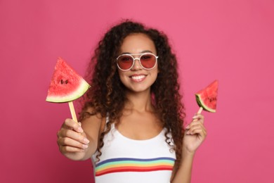 Beautiful young African American woman with pieces of watermelon against crimson background, focus on hand