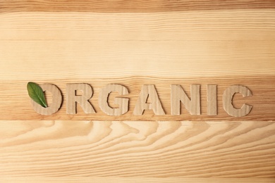 Photo of Word "Organic" made of cardboard letters and green leaf on wooden background, top view