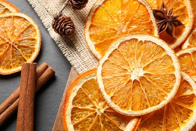 Photo of Many dry orange slices and spices on black textured table, flat lay