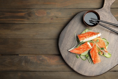 Fresh crab sticks with cucumber and soy sauce served on wooden table, flat lay. Space for text