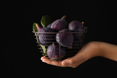 Woman holding basket with tasty raw figs on black background, closeup