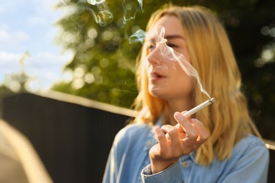 Photo of Young woman smoking cigarette outdoors, focus on hand. Space for text
