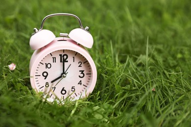 Pink alarm clock on green grass outdoors, space for text