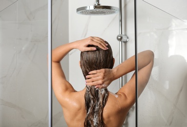 Young woman washing hair in shower at home, back view