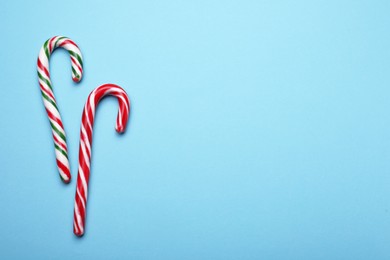 Two sweet Christmas candy canes on light blue background, flat lay. Space for text