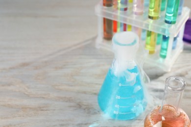 Photo of Laboratory glassware with colorful liquids and steam on white wooden table, space for text. Chemical reaction