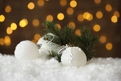 Beautiful Christmas balls and fir branch on snow against blurred festive lights