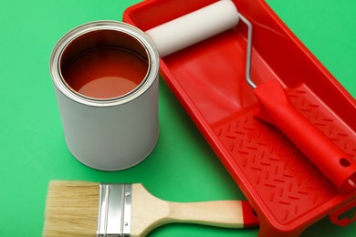 Photo of Can of orange paint, brush, roller and container on green background