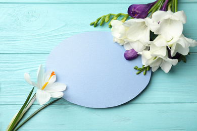 Beautiful spring flowers and blank card on blue wooden table, flat lay. Space for text