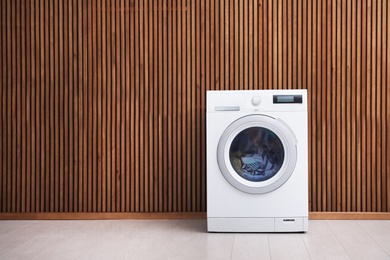 Washing machine with laundry near wooden wall. Space for text