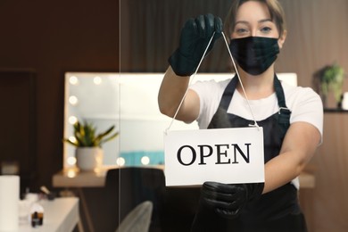 Woman hanging Open sign onto glass door in salon, focus on hands. Beauty services during Coronavirus quarantine