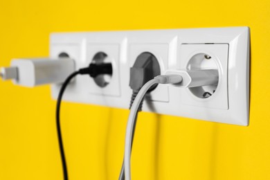 Power sockets with inserted plugs on yellow wall, closeup. Electrical supply