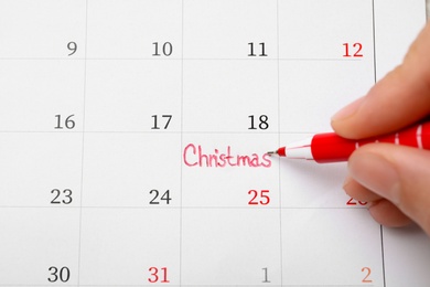 Woman writing word Christmas on calendar, top view. Holiday countdown