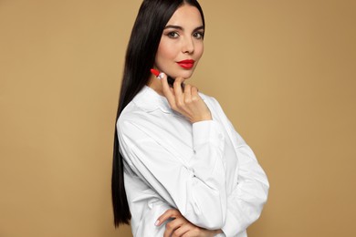 Young woman with beautiful makeup holding red lipstick on beige background
