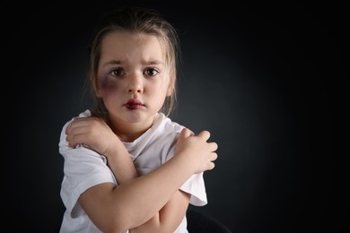 Little girl with bruises on face against dark background, space for text. Domestic violence victim