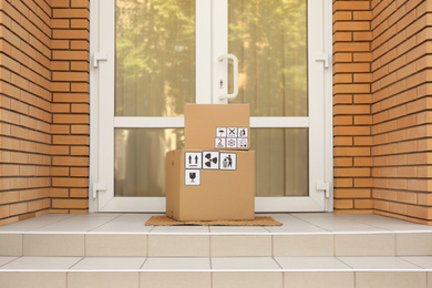 Cardboard boxes with different packaging symbols on door mat near entrance. Parcel delivery