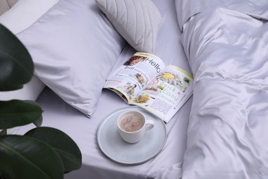 Cup of coffee and magazine on bed with soft silky bedclothes