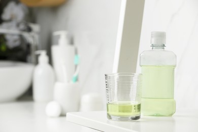 Bottle of mouthwash and glass on white shelf in bathroom, space for text