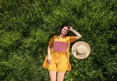 Beautiful young woman with book lying on green meadow, top view. Summer reading