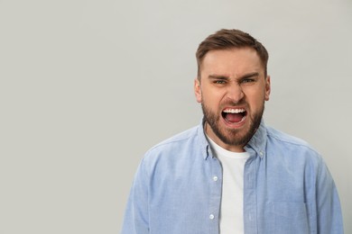 Angry young man on grey background, space for text. Hate concept