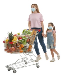 Mother and daughter in medical masks with shopping cart full of groceries on white background