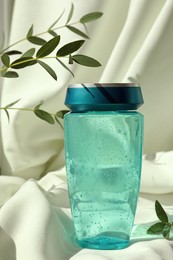 Photo of Bottle of hair care cosmetic product and green leaves on light fabric