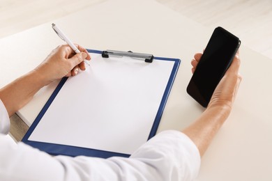 Photo of Doctor with smartphone and clipboard at desk, closeup. Online medicine concept