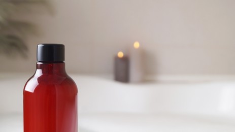 Red bottle of bath foam and candles indoors, closeup. Space for text