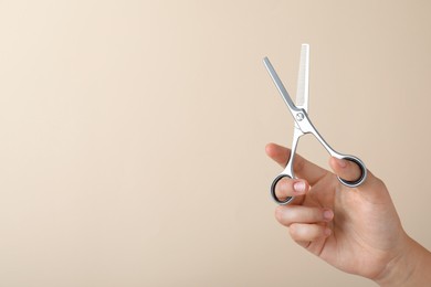 Hairdresser holding professional thinning scissors and space for text on beige background, closeup. Haircut tool