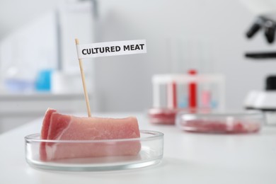 Petri dish with sample of lab grown pork labeled Cultured Meat on white table in laboratory. Space for text