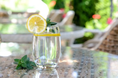 Photo of Refreshing water with lemon and mint on glass table in cafe, space for text