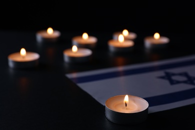 Burning candle and flag of Israel on black table. Holocaust memory day