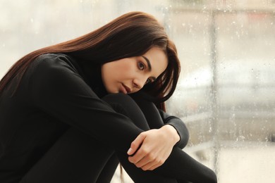 Depressed woman near window on rainy day