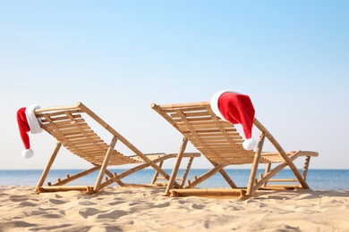 Photo of Sun loungers with Santa's hats on beach, space for text. Christmas vacation