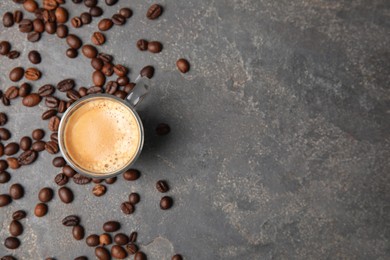 Cup of tasty espresso and scattered coffee beans on grey table, flat lay. Space for text