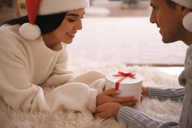 Couple holding Christmas gift box indoors, closeup