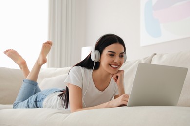 Woman with laptop and headphones lying on sofa at home