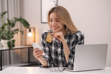 Woman with credit card using smartphone for online shopping at white table indoors