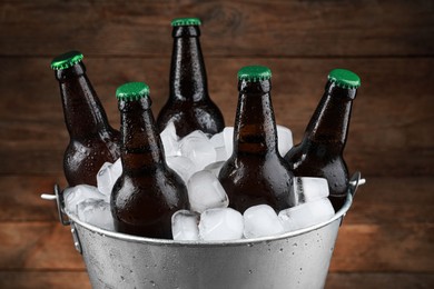 Photo of Metal bucket with bottles of beer and ice cubes on wooden background, closeup