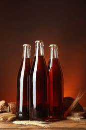 Photo of Bottles of delicious fresh kvass, spikelets and bread on wooden table