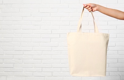 Woman with stylish blank eco bag near brick wall, closeup. Space for text