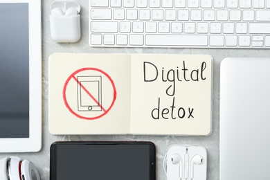 Flat lay composition of gadgets and notebook with words DIGITAL DETOX on light grey marble background